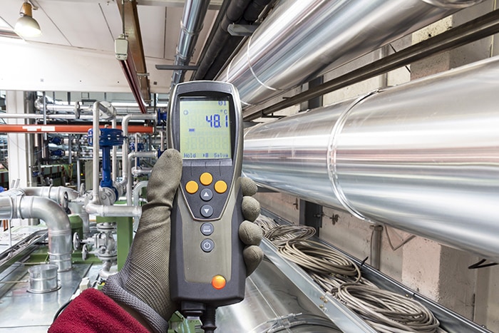 gloved hand holding sensor showing temperature of 48 degrees celsius within industrial setting