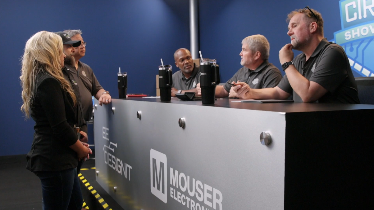 Circuit Showdown scene featuring show hosts convening at the judges table to deliberate with blue walls and branded logos behind them